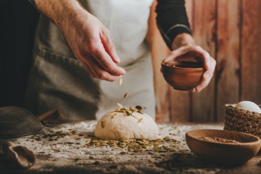 Tanınmayan genç bir adam koyu arkaplanda ayçiçeği ve kabak çekirdeği serpiştiriyor. Seçici odak.