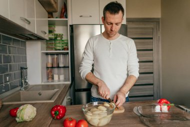 Tahtada patates kesen adam. Genç adam mutfakta sebze pişiriyor ve patates hazırlıyor. Seçici odak.