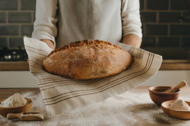 Havluda ya da peçetede ev yapımı tahıl ekmeği tutan önlüklü tanınmamış genç bir adam. Seçici odak.