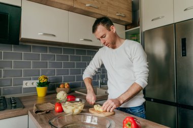 Tahtada patates kesen adam. Genç adam mutfakta sebze pişiriyor ve patates hazırlıyor. Seçici odak.