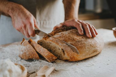 Unrecognizable young man in apron cutting homemade whole grain bread. Selective focus.
