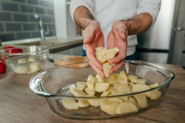 Adam patates doğradı ve onu fırın tabağına koydu. Mutfakta sebze pişiren tanınmamış bir adam. Erkeklerin ellerini kapat ve patatesi aşçıya hazırla. Seçici odak.