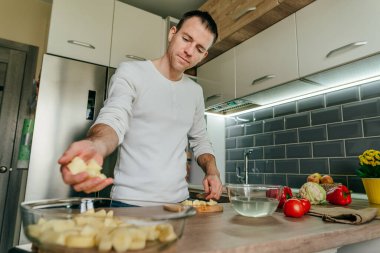Adam patates doğradı ve onu fırın tabağına koydu. Mutfakta sebze pişiren tanınmamış bir adam. Erkeklerin ellerini kapat ve patatesi aşçıya hazırla. Seçici odak.
