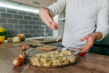 Adam soğan doğradı ve onu pişirme kabına koydu. Mutfakta sebze pişiren tanınmamış bir adam. Erkeklerin ellerini kapat ve aşçı için patates ve soğan hazırla. Seçici odak.