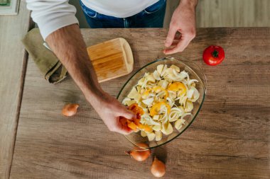 Adam dolmalık biberi kesiyor ve fırın kabına koyuyor. Mutfakta sebze pişiren tanınmamış bir adam. Erkeklerin elleri aşçı için patates ve dolmalık biber hazırlarken yakınlaşın. Seçici odak.