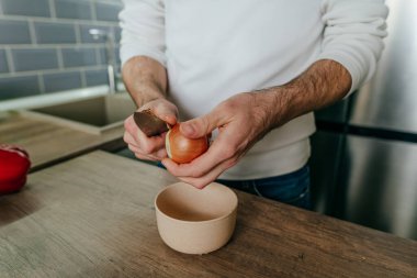 Soğan soyan adam. Mutfakta sebze pişiren tanınmamış bir adam. Erkeklerin ellerini kapat ve soğanı pişirmek için hazırla. Seçici odak.