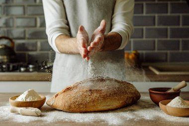 Önlüklü tanınmayan genç adam ahşap masaya un serpiştiriyor. Seçici odak.