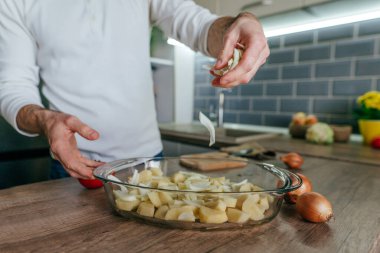 Adam soğan doğradı ve onu pişirme kabına koydu. Mutfakta sebze pişiren tanınmamış bir adam. Erkeklerin ellerini kapat ve aşçı için patates ve soğan hazırla. Seçici odak.
