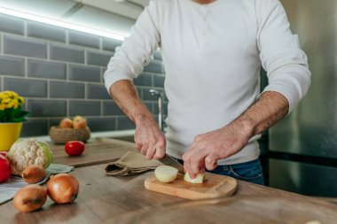 Soğan soyan adam. Mutfakta sebze pişiren tanınmamış bir adam. Erkeklerin ellerini kapat ve soğanı pişirmek için hazırla. Seçici odak.