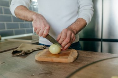 Soğan soyan adam. Mutfakta sebze pişiren tanınmamış bir adam. Erkeklerin ellerini kapat ve soğanı pişirmek için hazırla. Seçici odak.
