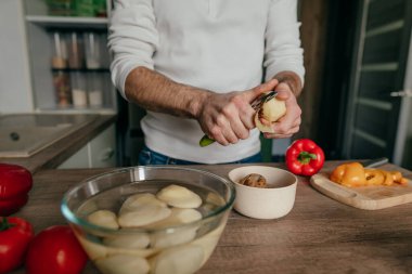 Patates soyan adam. Mutfakta sebze pişiren tanınmamış bir adam. Erkeklerin ellerini kapat ve patatesi aşçıya hazırla. Seçici odak.