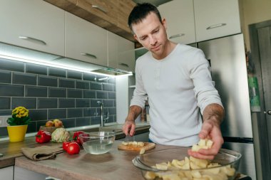 Adam patates doğradı ve onu fırın tabağına koydu. Mutfakta sebze pişiren tanınmamış bir adam. Erkeklerin ellerini kapat ve patatesi aşçıya hazırla. Seçici odak.