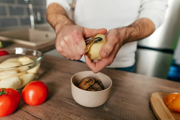 Man peeling potatoes. Unrecognizable man cooking vegetables in the kitchen. Close up of males hands preparing potato for cook. Selective focus.