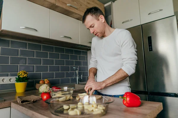 Man cutting potatoes on the board. Young man cooking vegetables in the kitchen preparing potato. Selective focus.