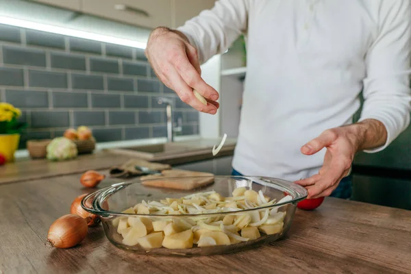 Adam soğan doğradı ve onu pişirme kabına koydu. Mutfakta sebze pişiren tanınmamış bir adam. Erkeklerin ellerini kapat ve aşçı için patates ve soğan hazırla. Seçici odak.