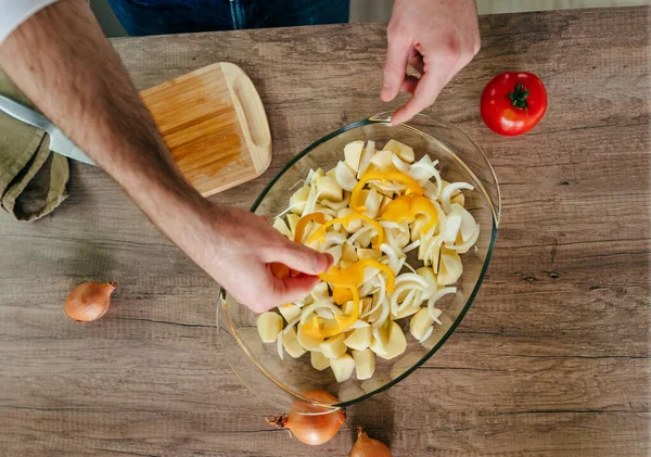 Adam dolmalık biberi kesiyor ve fırın kabına koyuyor. Mutfakta sebze pişiren tanınmamış bir adam. Erkeklerin elleri aşçı için patates ve dolmalık biber hazırlarken yakınlaşın. Seçici odak.