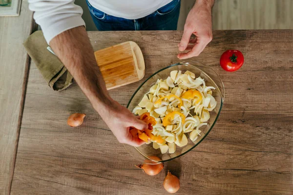 Adam dolmalık biberi kesiyor ve fırın kabına koyuyor. Mutfakta sebze pişiren tanınmamış bir adam. Erkeklerin elleri aşçı için patates ve dolmalık biber hazırlarken yakınlaşın. Seçici odak.