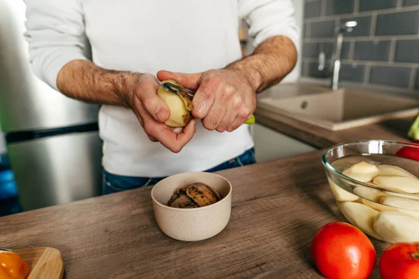 Patates soyan adam. Mutfakta sebze pişiren tanınmamış bir adam. Erkeklerin ellerini kapat ve patatesi aşçıya hazırla. Seçici odak.