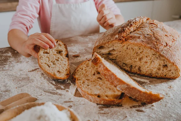 Önlüklü, elinde bir dilim ev yapımı tahıllı ekmek tutan tanınmamış küçük bir kız. Seçici odak.
