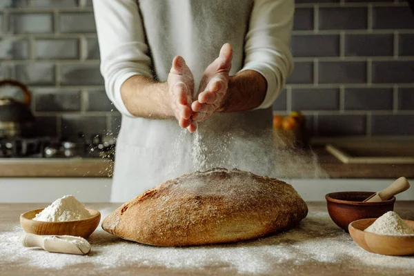 Önlüklü tanınmayan genç adam ahşap masaya un serpiştiriyor. Seçici odak.