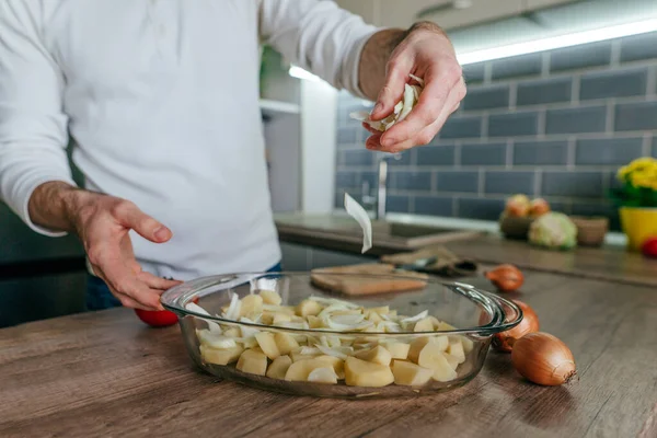 Adam soğan doğradı ve onu pişirme kabına koydu. Mutfakta sebze pişiren tanınmamış bir adam. Erkeklerin ellerini kapat ve aşçı için patates ve soğan hazırla. Seçici odak.
