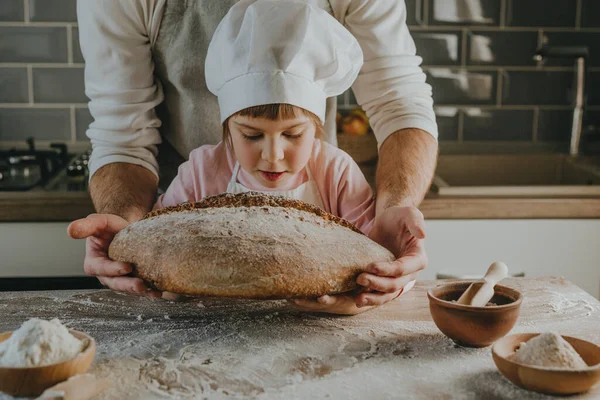 Önlüklü tanınmayan genç bir adam ve elinde kızıyla ev yapımı tahıl ekmeği tutuyor. Aile yemekleri konsepti. Seçici odak.