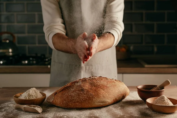 Önlüklü tanınmayan genç adam ahşap masaya un serpiştiriyor. Seçici odak.