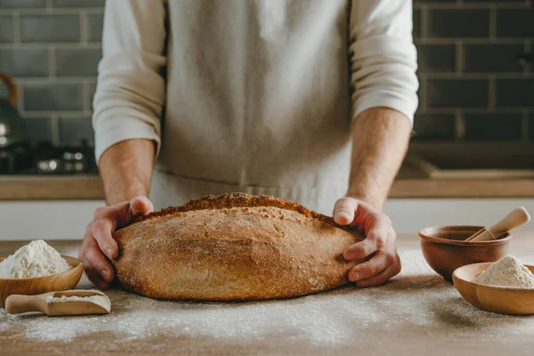 Önlüklü tanınmayan genç adam elinde tam tahıllı ekmek tutuyor. Seçici odak.