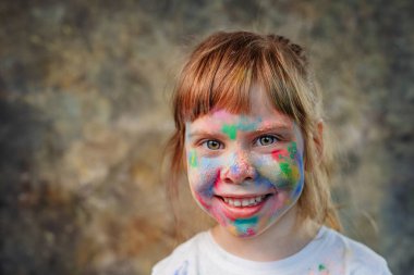Holi renkleriyle kaplı küçük bir kızın yüzü. Cildinde renkli resimlerle gülümseyen bir bebeğin portresi..