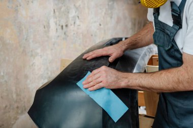 Erkek elinin zımpara kağıdıyla zımparalanmasına yakın bir araba tamponu. Arabanın plastik tampon kapağını boyamadan önceki ilk adım. Seçici odak.