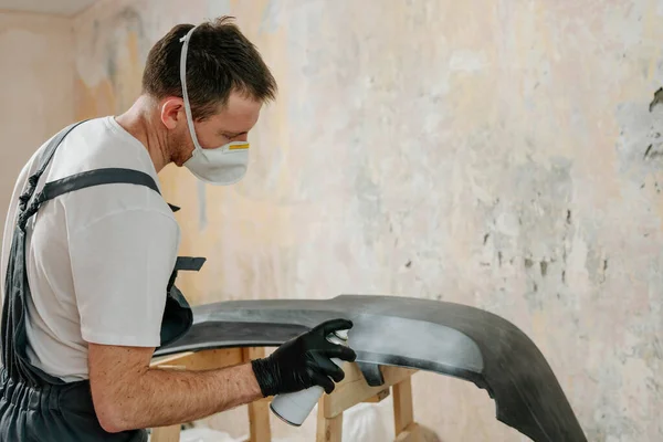 Young man painting a car bumper with spray can. Overhaul car's plastic