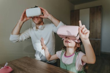 5 yaşındaki bir kız, evde oyun ve öğrenim için VR gözlüğü kullanarak babasıyla eğleniyor. Aile aktiviteleri konsepti. Aile tarafından kullanılan modern teknoloji. Seçici odak.