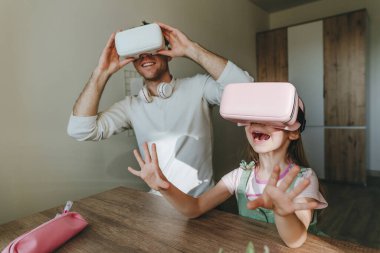 5 yaşındaki bir kız, evde oyun ve öğrenim için VR gözlüğü kullanarak babasıyla eğleniyor. Aile aktiviteleri konsepti. Aile tarafından kullanılan modern teknoloji. Seçici odak.