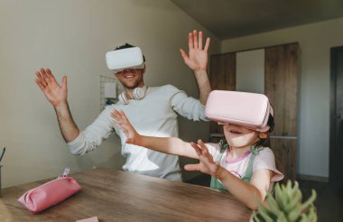 5 yaşındaki bir kız, evde oyun ve öğrenim için VR gözlüğü kullanarak babasıyla eğleniyor. Aile aktiviteleri konsepti. Aile tarafından kullanılan modern teknoloji. Seçici odak.