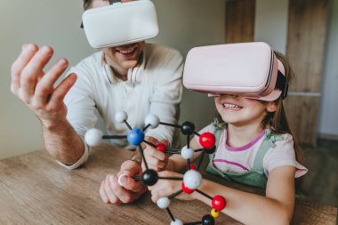 Küçük kız evde moleküler yapıyı öğrenmek için VR gözlüğü kullanarak babasıyla eğleniyor. Evde eğitim kavramı. Aile tarafından kullanılan modern teknoloji. Seçici odak.