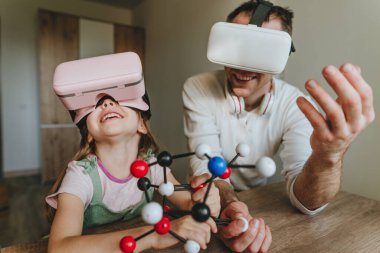 Küçük kız evde moleküler yapıyı öğrenmek için VR gözlüğü kullanarak babasıyla eğleniyor. Evde eğitim kavramı. Aile tarafından kullanılan modern teknoloji. Seçici odak.