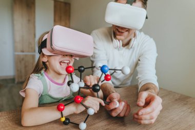 Küçük kız evde moleküler yapıyı öğrenmek için VR gözlüğü kullanarak babasıyla eğleniyor. Evde eğitim kavramı. Aile tarafından kullanılan modern teknoloji. Seçici odak.