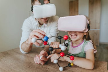 Küçük kız evde moleküler yapıyı öğrenmek için VR gözlüğü kullanarak babasıyla eğleniyor. Evde eğitim kavramı. Aile tarafından kullanılan modern teknoloji. Seçici odak.