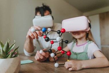 Küçük kız evde moleküler yapıyı öğrenmek için VR gözlüğü kullanarak babasıyla eğleniyor. Evde eğitim kavramı. Aile tarafından kullanılan modern teknoloji. Seçici odak.