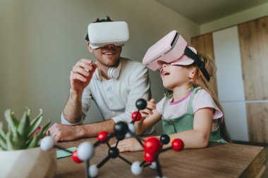 Küçük kız evde moleküler yapıyı öğrenmek için VR gözlüğü kullanarak babasıyla eğleniyor. Evde eğitim kavramı. Aile tarafından kullanılan modern teknoloji. Seçici odak.