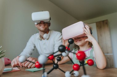 Küçük kız evde moleküler yapıyı öğrenmek için VR gözlüğü kullanarak babasıyla eğleniyor. Evde eğitim kavramı. Aile tarafından kullanılan modern teknoloji. Seçici odak.