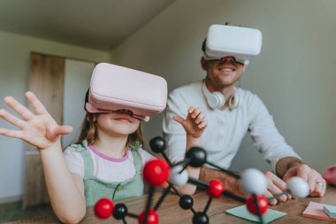 Küçük kız evde moleküler yapıyı öğrenmek için VR gözlüğü kullanarak babasıyla eğleniyor. Evde eğitim kavramı. Aile tarafından kullanılan modern teknoloji. Seçici odak.