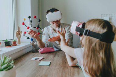 Kızının sanal gerçeklik gözlüğü kullanan bir molekülün yapısını tarif eden genç bir adam. Aile tarafından kullanılan modern teknoloji. Evde eğitim kavramı. Seçici odak.