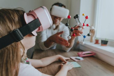 Kızının sanal gerçeklik gözlüğü kullanan bir molekülün yapısını tarif eden genç bir adam. Aile tarafından kullanılan modern teknoloji. Evde eğitim kavramı. Seçici odak.