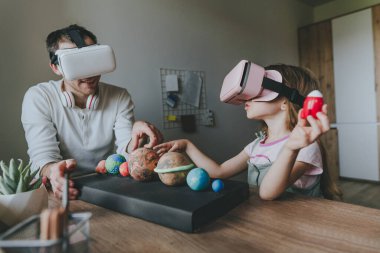 Küçük kız evde güneş sistemi gezegenlerini öğrenmek için VR gözlüğü kullanarak babasıyla eğleniyor. Evde eğitim kavramı. Aile tarafından kullanılan modern teknoloji. Seçici odak.