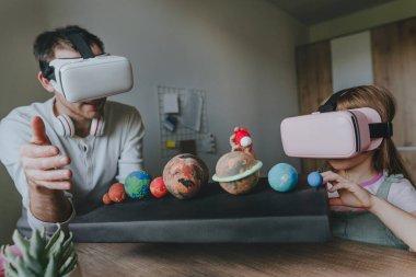 Küçük kız evde güneş sistemi gezegenlerini öğrenmek için VR gözlüğü kullanarak babasıyla eğleniyor. Evde eğitim kavramı. Aile tarafından kullanılan modern teknoloji. Seçici odak.