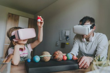 Küçük kız evde güneş sistemi gezegenlerini öğrenmek için VR gözlüğü kullanarak babasıyla eğleniyor. Evde eğitim kavramı. Aile tarafından kullanılan modern teknoloji. Seçici odak.