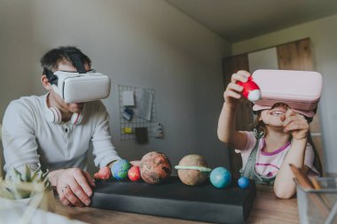 Küçük kız evde güneş sistemi gezegenlerini öğrenmek için VR gözlüğü kullanarak babasıyla eğleniyor. Evde eğitim kavramı. Aile tarafından kullanılan modern teknoloji. Seçici odak.