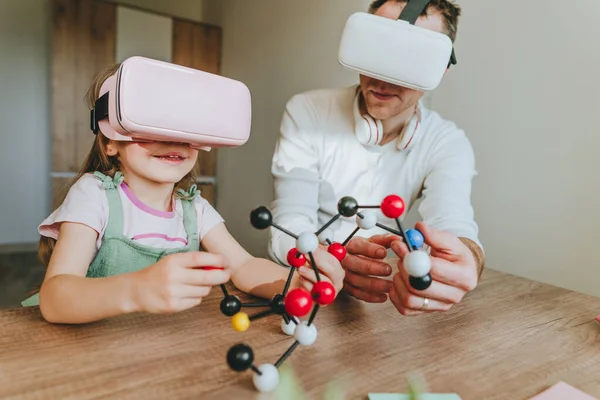 Küçük kız evde moleküler yapıyı öğrenmek için VR gözlüğü kullanarak babasıyla eğleniyor. Evde eğitim kavramı. Aile tarafından kullanılan modern teknoloji. Seçici odak.