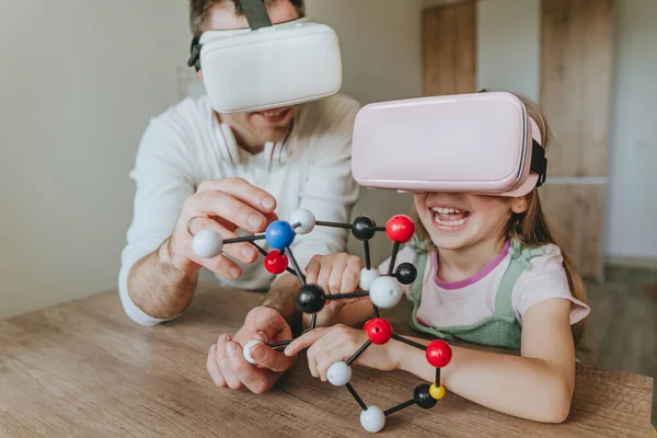 Küçük kız evde moleküler yapıyı öğrenmek için VR gözlüğü kullanarak babasıyla eğleniyor. Evde eğitim kavramı. Aile tarafından kullanılan modern teknoloji. Seçici odak.